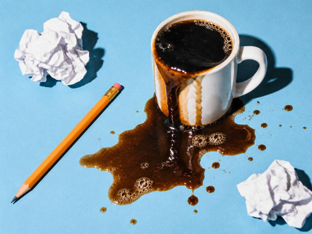 Spilled coffee beside a pencil and crumpled paper on a blue tabletop