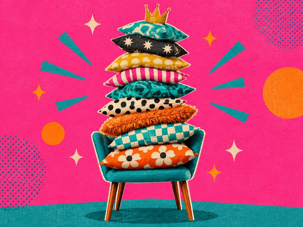 A towering stack of mismatched pillows on a teal armchair, topped with a crown
